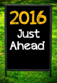 2016 JUST AHEAD  message on sidewalk blackboard sign against green grass background. Copy Space available. Concept image