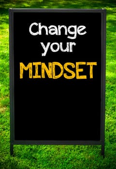 CHANGE YOUR MINDSET  message on sidewalk blackboard sign against green grass background. Copy Space available. Concept image