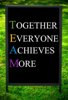 TOGETHER EVERYONE ACHIEVES MORE  message on sidewalk blackboard sign against green grass background. Copy Space available. Concept image