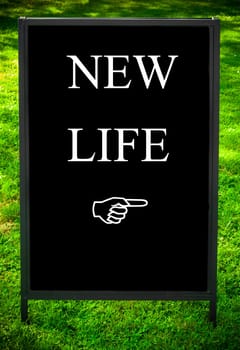 NEW LIFE message and hand pointing to the right on sidewalk blackboard sign against green grass background. Copy Space available. Concept image