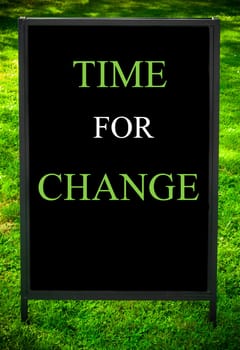TIME FOR CHANGE  message on sidewalk blackboard sign against green grass background. Copy Space available. Concept image