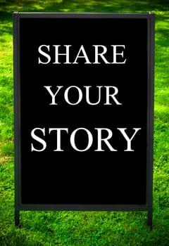 SHARE YOUR STORY  message on sidewalk blackboard sign against green grass background. Copy Space available. Concept image