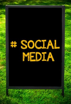 Hashtag Social Media message on sidewalk blackboard sign against green grass background. Copy Space available. Concept image