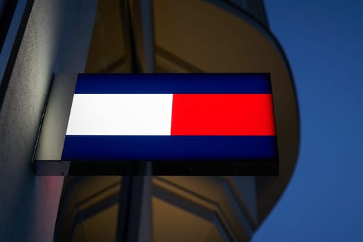 Neon light with the logo of fashion designer Tommy Hilfiger in a shopping street in Berlin in the evening