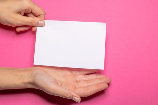 female hand holds a blank piece of paper with copy space in front of a Hot Pink background cardboard with the hand making a presenting gesture