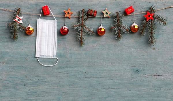 Corona and Christmas. A protective mask hangs next to Christmas tree balls, fir branches and gift packages
