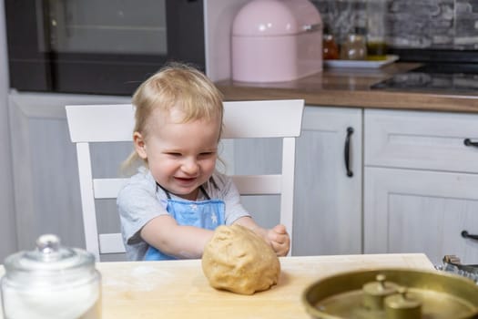 Little boy rejoices over the finished dough for sweet pastries in the kitchen.