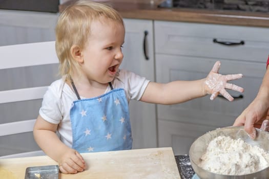 Little helper. Little cute boy shows his hands soiled from flour in domestic kitchen. Horizontally.
