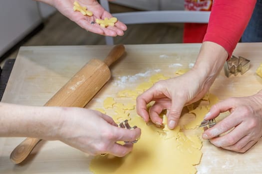 Two women cut out cookies from dough in domestic kitchen, indoors. Horizontally.