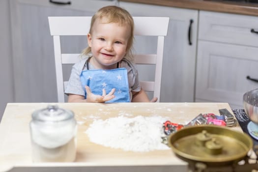 Llittle cute boy is posing at the table ready to bake cookies in the kitchen.