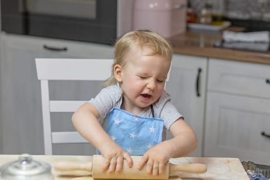 Little boy "suffers"" while working with a wooden kitchen roller in domestic kitchen. Horizontally."