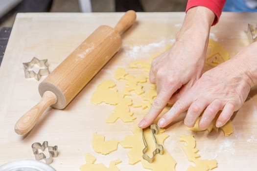 Female hands cut out dog-shaped cookies from the dough in domestic kitchen. Horizontally.