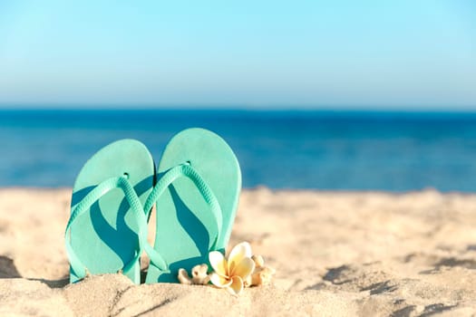 Turquoise or light blue flip flops or sandal shoe stuck in the sand on sandy beach by the sea coastline or ocean. Travel or vacation concept in hot countries in summer or winter. High quality photo