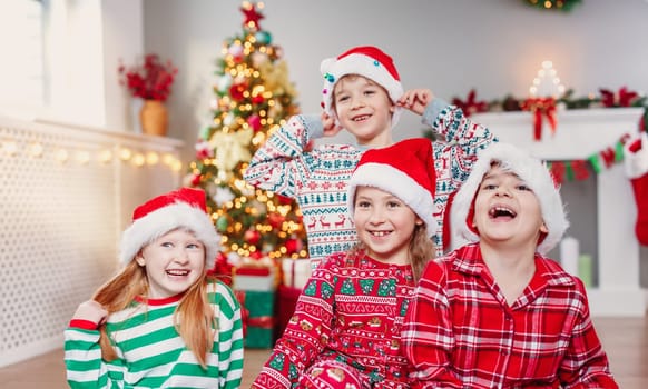 Happy children sitting in the living room at home in christmas pajamas. Xmas concept. Smiling boys and girls indoors