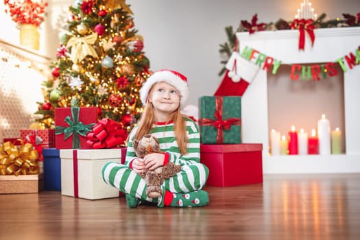 Cute little girl sitting in the room with christmas decoration. Child near christmas tree