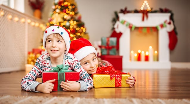 Happy children lying in the living room at home in christmas pajamas. Xmas concept. Smiling boy and girl indoors