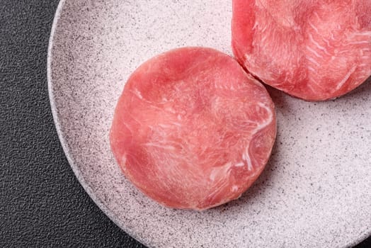 Two fresh slices of raw tuna fillet with spices and herbs on a dark concrete background
