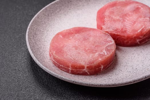 Two fresh slices of raw tuna fillet with spices and herbs on a dark concrete background