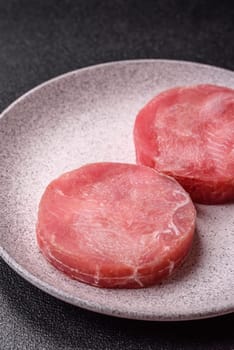 Two fresh slices of raw tuna fillet with spices and herbs on a dark concrete background