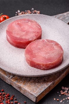 Two fresh slices of raw tuna fillet with spices and herbs on a dark concrete background