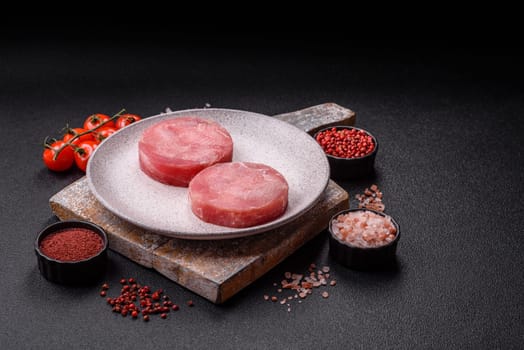 Two fresh slices of raw tuna fillet with spices and herbs on a dark concrete background