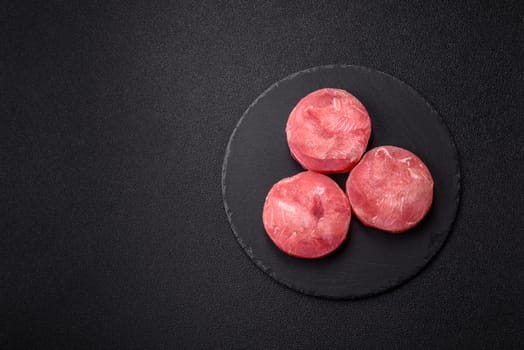 Two fresh slices of raw tuna fillet with spices and herbs on a dark concrete background