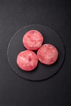 Two fresh slices of raw tuna fillet with spices and herbs on a dark concrete background