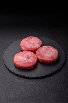 Two fresh slices of raw tuna fillet with spices and herbs on a dark concrete background