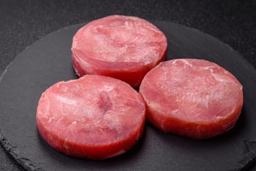Two fresh slices of raw tuna fillet with spices and herbs on a dark concrete background