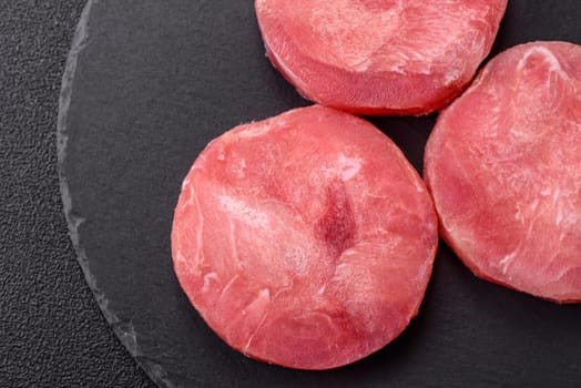 Two fresh slices of raw tuna fillet with spices and herbs on a dark concrete background