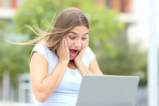 Amazed teen checking laptop in a park