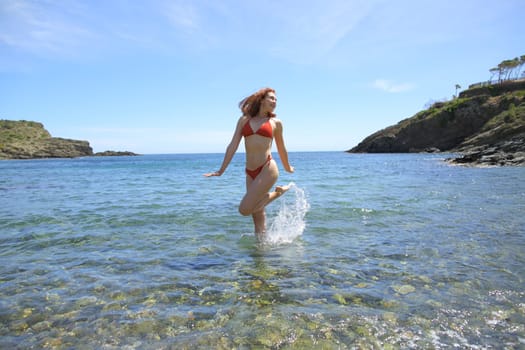 Woman in bikini twirling in the water on the beach