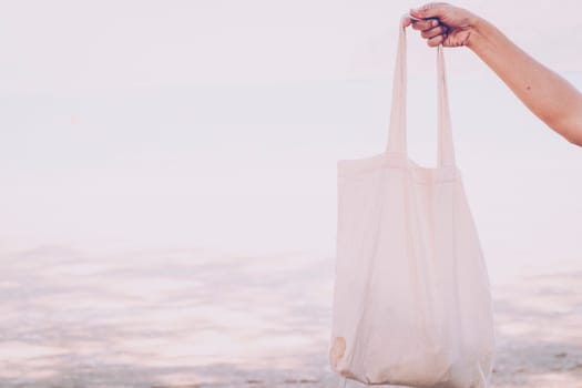 White blank cotton eco tote. Design mockup. Holding blank canvas tote bag, design mockup. Handmade shopping tote bag for girls. Beach background. Summer idea