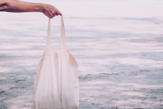 White blank cotton eco tote. Design mockup. Holding blank canvas tote bag, design mockup. Handmade shopping tote bag for girls. Beach background. Summer idea