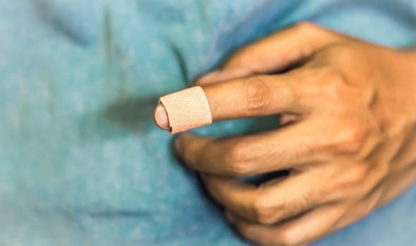 Close up of a bandage on a man's index finger against blue background. Health care first aid emergency recovery.