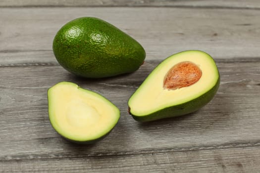 Avocado cut in half with whole pear in back, on gray wood table.