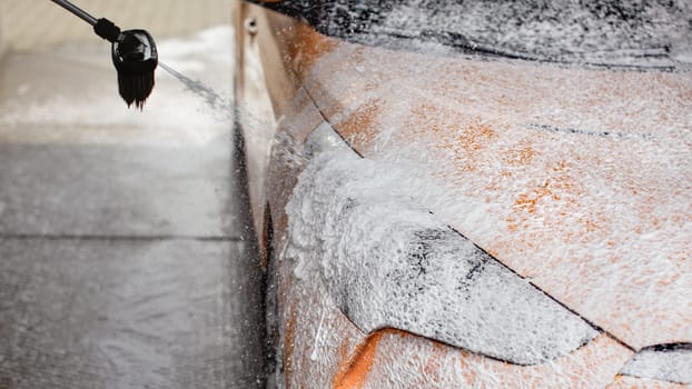 Car being washed at self service carwash. Foam and shampoo spray drops from the brush to headlight.