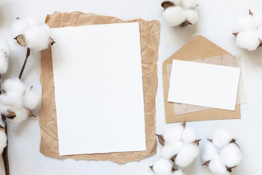 Feminine Wedding cards mockup on white table with cotton flowers top view. Elegant modern template with horizontal blank paper card, flat lay with place for text. Minimalistic stationery scene. Natural, eco-friendly concept