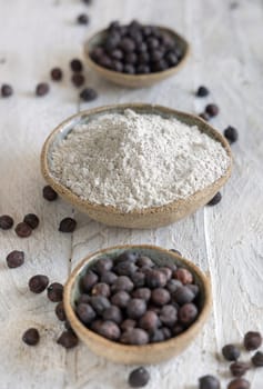 Bowls of black chickpea flour and wooden spoon of beans closeup on white wooden table. Traditional beans from Apulia and Basilicata in Italy
