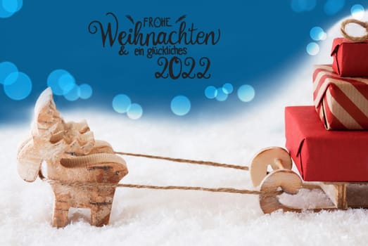 Reindeer With Sled And Christmas Gifts And Snow. Blue Sparkling Background With German Calligraphy Frohe Weihnachten Und Ein Glueckliches 2022 Means Merry Christmas And A Happy 2022