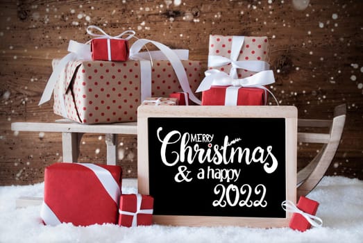 Blackboard With English Calligraphy Merry Christmas And A Happy 2022. Sled With Christmas Gift And Presents. Wooden Background With Snow And Snowflakes