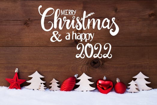 English Calligraphy Merry Christmas And A Happy 2022. Red Christmas Decoration Like Tree And Ball Ornament. Wooden Background With Snow