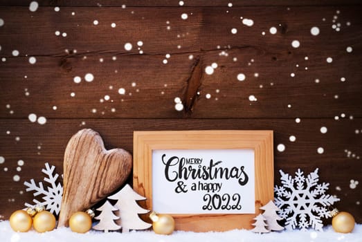 English Calligraphy Merry Christmas And Happy 2022. Golden Christmas Ornament Like Ball, Heart And Tree. Wooden Background With Snow And Snowflakes