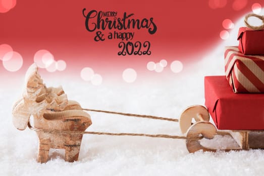 Reindeer With Sled And Christmas Gifts And Snow. Red Sparkling Background With English Calligraphy Merry Christmas And A Happy 2022
