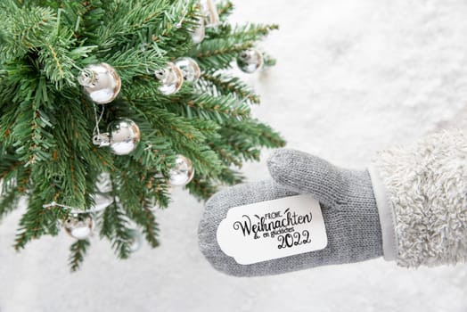Glove With Label With German Calligraphy Frohe Weihnachten Und Ein Glueckliches 2022 Means Merry Christmas And Happy 2022. Christmas Tree With Silver Ball Ornament And Snow