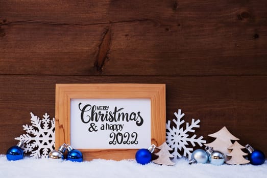 English Calligraphy Merry Christmas And Happy 2022. Blue Christmas Ornament Like Tree, Snowflake And Ball. Wooden Background With Snow
