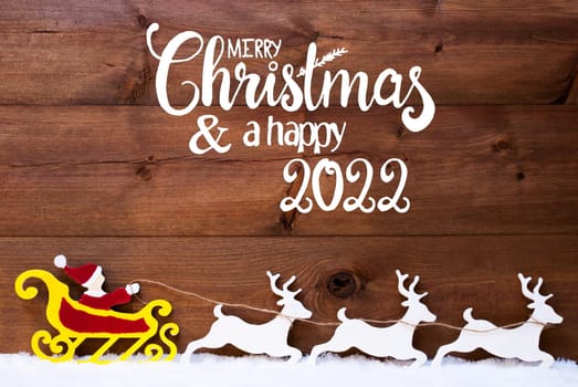 English Calligraphy Merry Christmas And Happy 2022. Santa Claus With Sleigh And Reindeers. Wooden Background With Snow