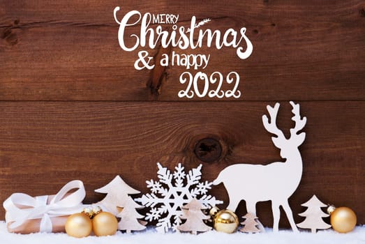 English Calligraphy Merry Christmas And A Happy 2022. Golden Christmas Decoration Like Tree, Gift, Ball And Reindeer. Wooden Background With Snow