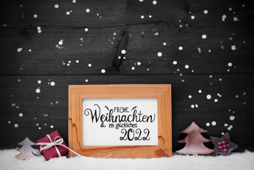 Frame With German Calligraphy Frohe Weihnachten Und Ein Glueckliches 2022 Means Merry Christmas And A Happy 2022. Christmas Decoration Like Gift, Tree And Star. Gray Wooden Background With Snowflakes