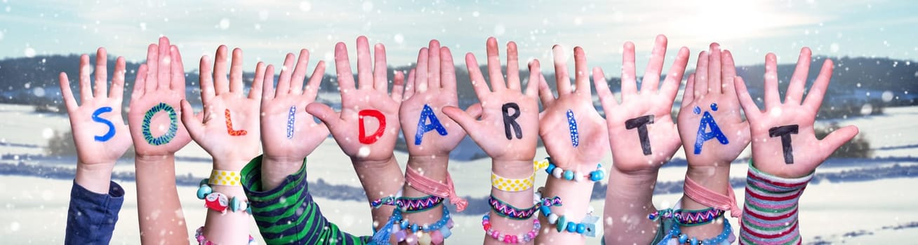 Kids Hands Holding Colorful German Word Solidaritaet Means Solidarity. Snowy Winter Background With Snowflakes